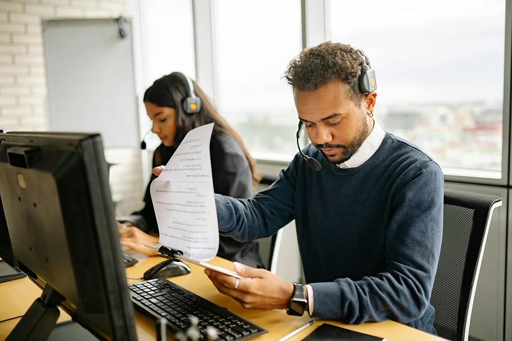 Office professionals using headsets and reviewing documents at computers
